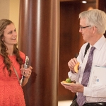 A man holding a plate of fruit and a women holding a cup are speaking to eachother at the reception